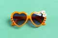 Stylish orange sunglasses in heart shape on mentol green background, flat lay.