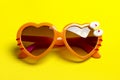 Stylish orange sunglasses in heart shape on yellow background, flat lay. Royalty Free Stock Photo