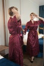 Stylish pin up short hair blonde woman with plus size curvy body posing in fashion red bathrobe near the mirror in the Royalty Free Stock Photo