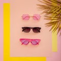 Stylish pink sunglasses collection. Summer funky glasses on pink background with gold palm leaves. Top View. Flat lay