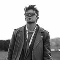 Stylish portrait cool young hipster man in fashionable dark sunglasses in vintage leather black jacket with trendy hairstyle Royalty Free Stock Photo