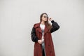 Stylish portrait urban young woman with long hair in fashionable spring youth trench coat in trendy sunglasses near vintage wall