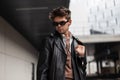 Stylish portrait of a young man hipster in sunglasses with a fashionable hairstyle in trendy black clothes near gray building on Royalty Free Stock Photo