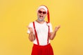 Stylish positive adult man in santa claus hat and sunglasses holding fingers like pistols, having fun celebrating holidays