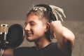 Stylish positive guy with dreadlocks is recording a song in the studio. A young attractive singer in black studio headphones