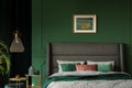 Stylish poster above comfortable king size bed with headboard in dark green bedroom