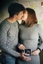 Stylish pregnant couple holding ultrasound scan of baby on baby bump and kissing. Young parents, happy mom and dad, holding in Royalty Free Stock Photo