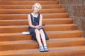 Stylish preteen girl using a phone sitting on a rusty staircase. Child and gadget concept.