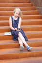 Stylish preteen girl using a phone sitting on a rusty staircase. Child and gadget concept.