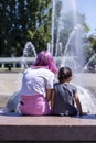 Stylish PreTeen sitting with child watching fountain. Royalty Free Stock Photo