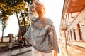 Stylish pretty blonde woman in fashion jeans casual clothes walks down the street against the backdrop of a bright sunset. Back Royalty Free Stock Photo