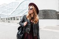 Stylish pretty young hipster woman in purple elegant hat in a vintage leather jacket with a fashionable backpack Royalty Free Stock Photo