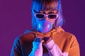 Stylish teen girl in glasses blow bubble gum look at camera purple background Royalty Free Stock Photo