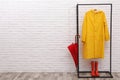 Stylish rack with umbrella, raincoat and rubber boots near white brick wall. Space for text Royalty Free Stock Photo