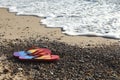 Stylish rainbow flip flops on pebbles near sea. Space for text