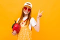 Stylish red-haired girl with a red handbag in the shape of an apple on a yellow background