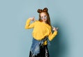 Teenager girl in yellow sweatshirt and black skirt poses as a top model pointing fingers at herself with both hands