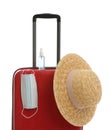 Stylish red suitcase with hat, antiseptic spray and protective mask on white background. Travelling during coronavirus pandemic