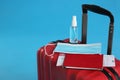 Stylish red suitcase with protective mask, antiseptic spray, passport and ticket on light blue background