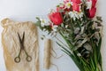 Stylish red tulips, daffodils bouquet and craft paper, scissors and twine on rustic white wood Royalty Free Stock Photo