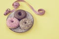 Stylish retro dish with delicious pink and chocolate donuts and a tailor`s meter on yellow background. Concept of diet