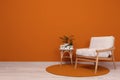 Stylish room interior with armchair and green plants near orange wall, space for text Royalty Free Stock Photo