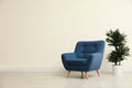 Stylish room interior with comfortable armchair and plant near beige wall Royalty Free Stock Photo