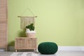 Stylish room interior with knitted pouf, wooden furniture and plant near light green wall, space for text