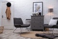 Stylish room interior with grey chest of drawers and chairs near white brick wall Royalty Free Stock Photo