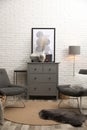 Stylish room interior with grey chest of drawers and chairs near white brick wall Royalty Free Stock Photo