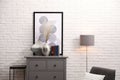 Stylish room interior with grey chest of drawers near white brick wall