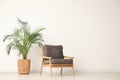 Stylish room interior with wooden armchair and houseplant near light wall Royalty Free Stock Photo