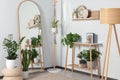 Stylish room interior with wooden furniture, houseplants and full length mirror near white wall Royalty Free Stock Photo
