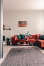 Stylish round table with flowers next to corner sofa with emerald pillows