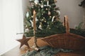 Stylish rustic basket with fir branches, vintage candle and wooden star on table against festive decorated christmas tree in Royalty Free Stock Photo