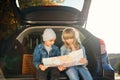 Agreeable boy and girl are looking at the road map while sitting in the auto`s trunk and discussing the move direction Royalty Free Stock Photo