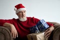 Stylish Santa. Middle aged man with beard wearing Christmas hat and red sweater looking away, holding gift boxes while Royalty Free Stock Photo