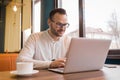 Stylish satisfied young businessman of European appearance in glasses, with a beard, in a white shirt looks into a laptop while