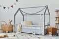 Stylish scandinavian child`s room with creative wooden bed, rattan basket, wooden shelf, plush, wooden toys and hanging textile.