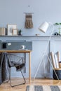 Stylish scandinavian home office with wooden desk, chair, design lamp, office supplies, black basket, plant.