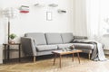 Stylish scandinavian interior of living room with small design table ,sofa, lamp and shelfs. White walls, plants on the windowsill Royalty Free Stock Photo