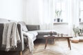 Stylish scandinavian interior of living room with small design table ,sofa, lamp and shelfs. White walls, plants on the windowsill Royalty Free Stock Photo