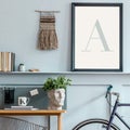 Stylish scandinavian living room with mock up poster frame on the shelf, wooden desk, bicycle, office supplies and personal.