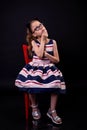 Stylish schoolgirl in a fluffy dress sits on a chair, filmed on a black background