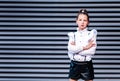 Stylish schoolgirl in a white blouse, black shorts posing against the backdrop of metal blinds