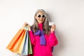 Stylish senior asian woman in sunglasses going shopping on holiday sale, holding paper bags and plastic credit card Royalty Free Stock Photo