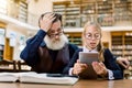 Stylish senior man with his granddaughter is using a digital tablet in the library. Girl reads information from tablet Royalty Free Stock Photo