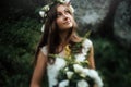 Stylish sensual boho bride with bouquet on background of rocks and woods