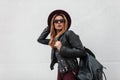Stylish sexy young hipster woman in purple elegant hat in a vintage leather jacket with a fashionable backpack Royalty Free Stock Photo