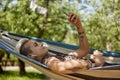 Young diverse female lying in a hammock in a green garden and listening to music in wireless headphones. Beautiful tattooed woman Royalty Free Stock Photo